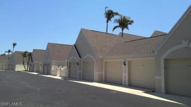 View of front facade with a shingled roof, stucco siding, community garages, and a residential view