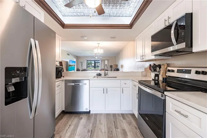Kitchen featuring stainless steel appliances, ornamental molding, white cabinetry, light countertops, and light wood-type flooring