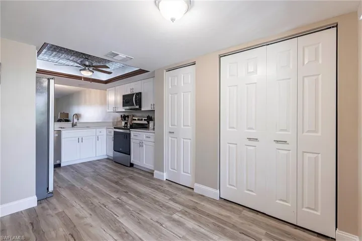 Kitchen with stainless steel appliances, light wood-type flooring, light countertops, white cabinetry, and a tray ceiling
