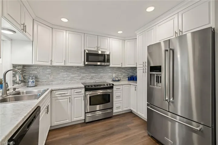 Kitchen featuring sink, white cabinets, decorative backsplash, light stone counters, and stainless steel appliances
