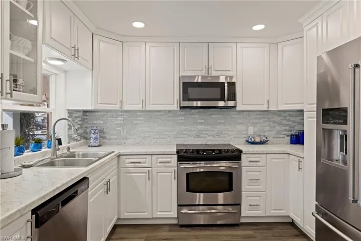 Kitchen featuring sink, dark wood-type flooring, appliances with stainless steel finishes, tasteful backsplash, and white cabinets