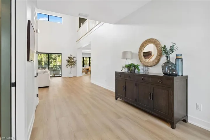 Hall with light wood-style flooring, healthy amount of natural light, baseboards, and a high ceiling