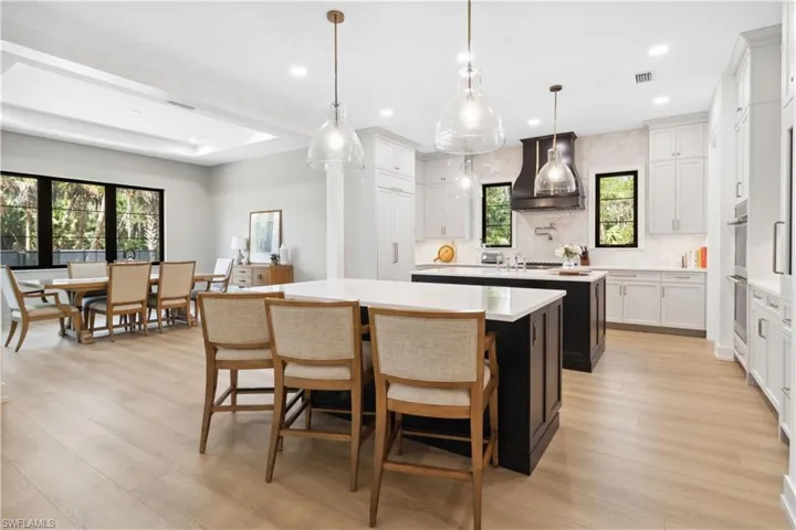 Kitchen featuring custom exhaust hood, a kitchen island with sink, light countertops, recessed lighting, and tasteful backsplash