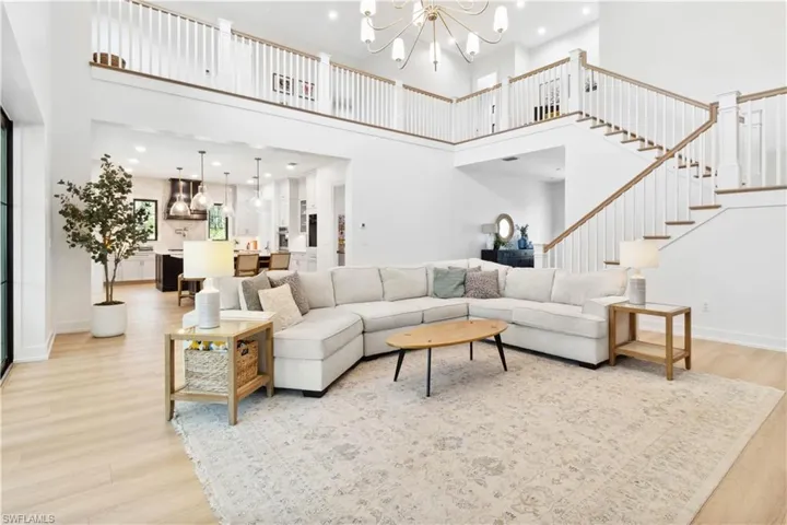 Living area with light wood finished floors, a chandelier, a towering ceiling, stairs, and recessed lighting