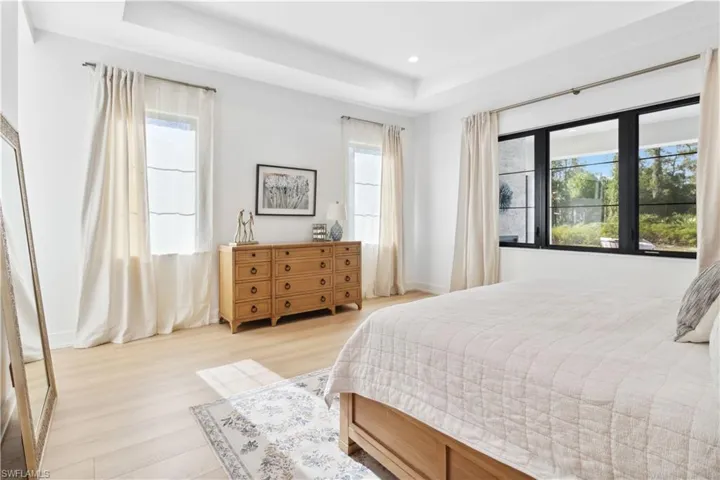 Bedroom featuring a raised ceiling, light wood-style floors, recessed lighting, and baseboards