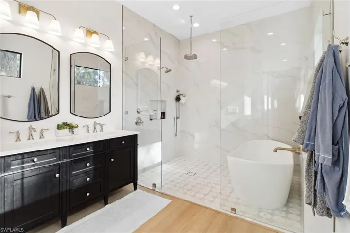 Bathroom featuring a marble finish shower, wood finished floors, double vanity, a soaking tub, and recessed lighting