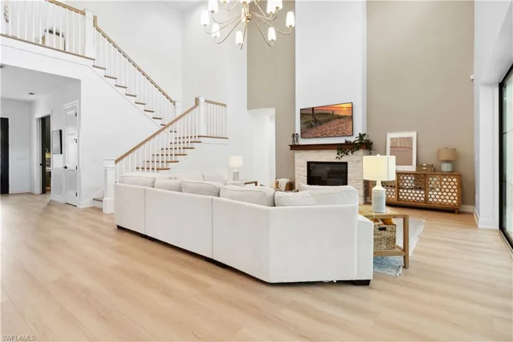 Living area with a high ceiling, light wood-type flooring, a glass covered fireplace, stairway, and a chandelier