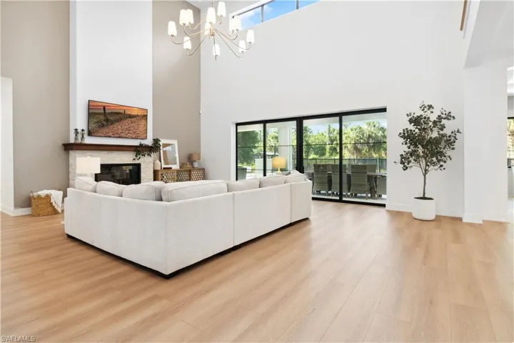 Living area featuring a towering ceiling, light wood-type flooring, baseboards, a chandelier, and a glass covered fireplace