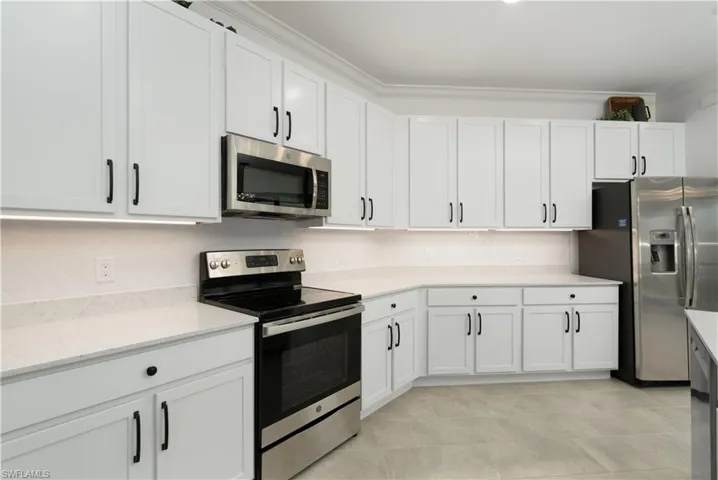 Kitchen with appliances with stainless steel finishes, white cabinets, ornamental molding, and decorative backsplash