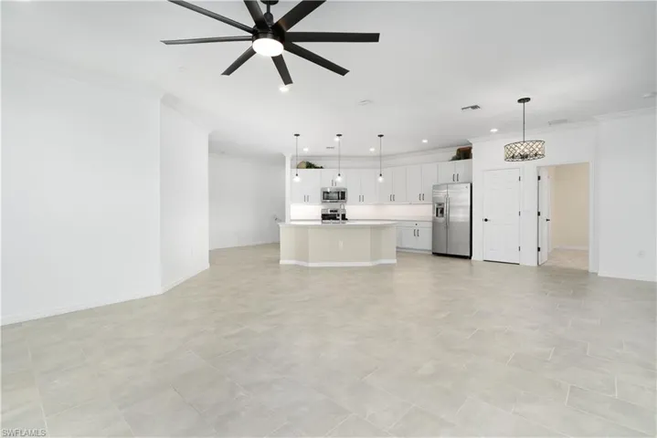 Unfurnished living room with ornamental molding, visible vents, baseboards, and a ceiling fan