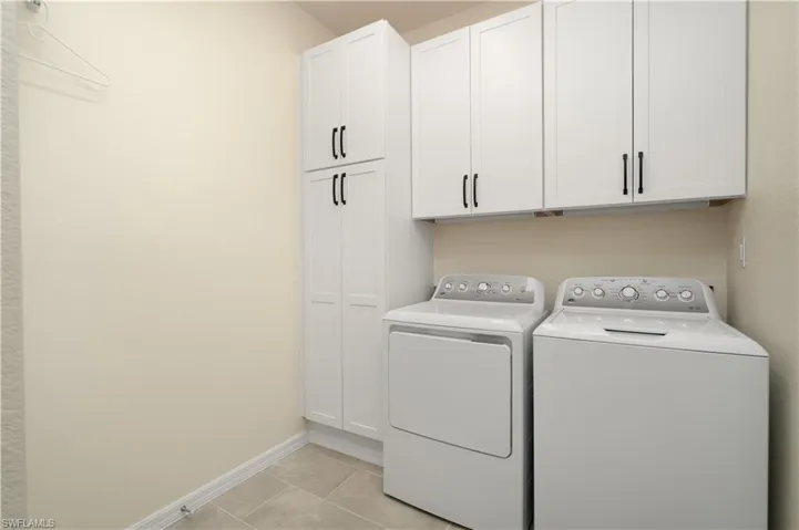 Laundry area featuring light tile patterned flooring, washing machine and clothes dryer, cabinet space, and baseboards