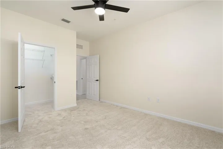 Unfurnished bedroom with a closet, a walk in closet, visible vents, and light colored carpet