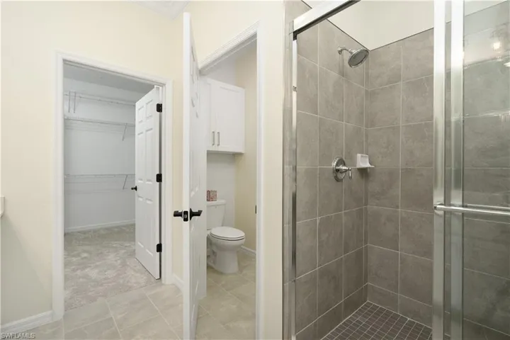 Bathroom with toilet, a shower stall, a spacious closet, and tile patterned flooring