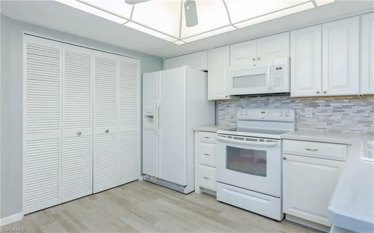 Kitchen featuring white cabinetry, light hardwood / wood-style floors, white appliances, and backsplash
