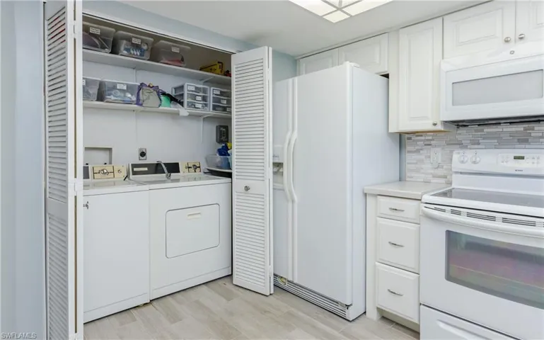 Kitchen featuring tasteful backsplash, white cabinetry, washing machine and clothes dryer, light hardwood / wood-style floors, and white appliances