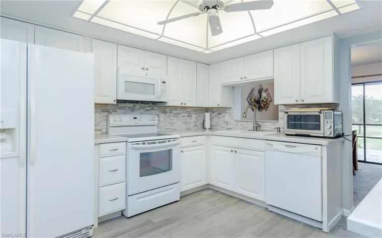 Kitchen with white cabinets, white appliances, ceiling fan, and sink