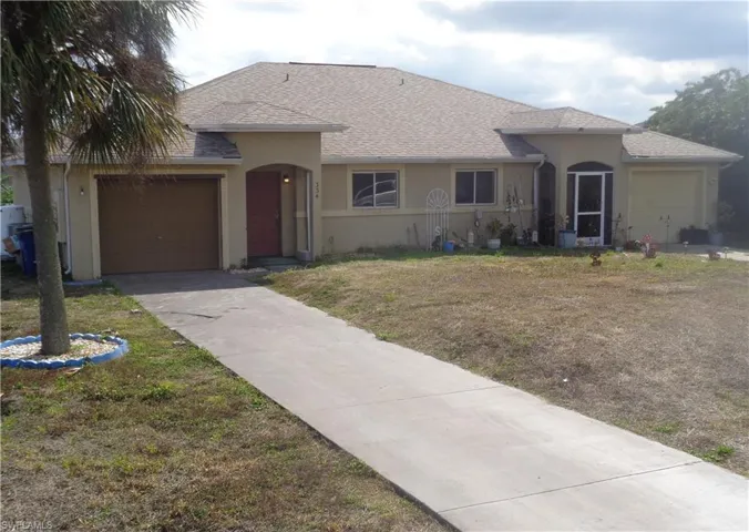 Left view of front of the duplex with a garage for each unit, roof with shingles, stucco siding, a front yard, and concrete driveway