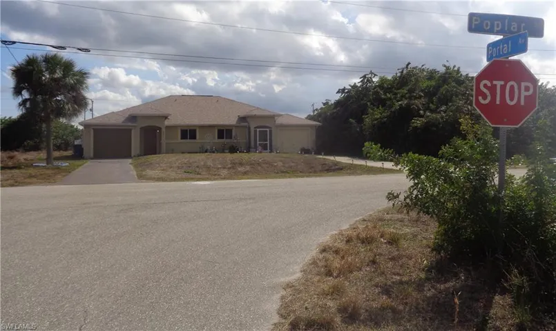 Wide angle view of the front of the duplex with an attached garage for each unit, stucco siding, and driveway. Duplex located in the intersection pf Poplar Street and Portal Avenue