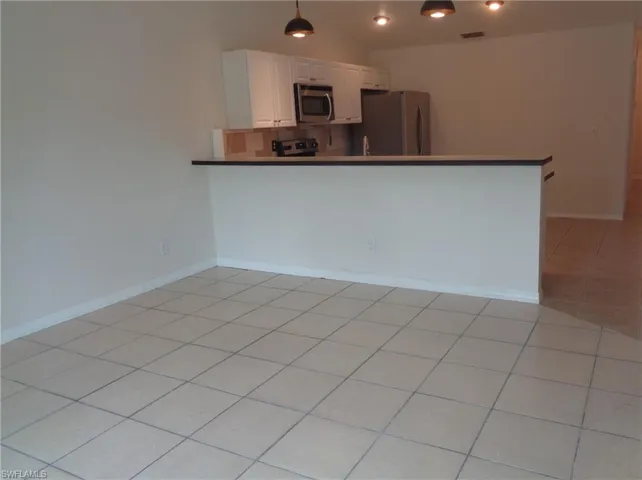 Dining area with light color tile floors. Kitchen can be seen in the back