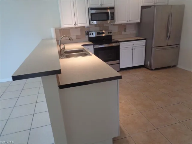 Kitchen with white cabinets, stainless steel appliances, and light tile patterned flooring