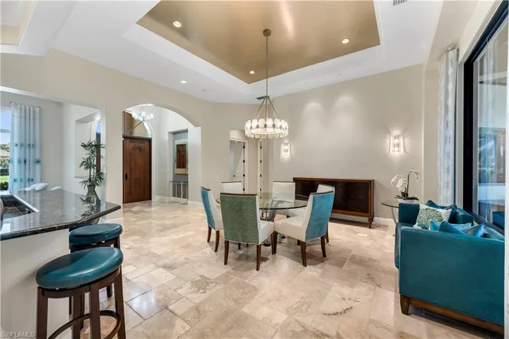 Tray ceiling with gold-finish accent, textured tile flooring, built-in counter with dark countertop, large sliding glass door, and arched doorway