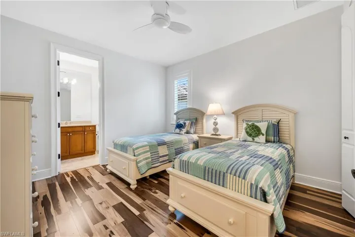 Wood-finish flooring, ceiling fan, white window shutters, and an attached bathroom with a single vanity and wall-mounted lighting