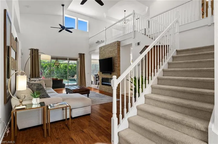 Living area with stairs, ceiling fan, dark wood finished floors, a stone fireplace, and a high ceiling