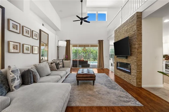 Living area with healthy amount of natural light, a stone fireplace, a ceiling fan, wood finished floors, and high vaulted ceiling