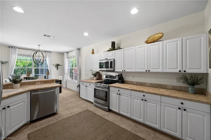 Kitchen with stainless steel appliances, white cabinetry, a chandelier, hanging light fixtures, and recessed lighting