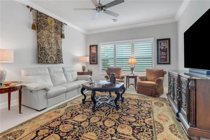 Carpeted living room with ceiling fan, ornamental molding, visible vents, and baseboards