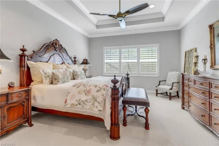 Bedroom with light carpet, baseboards, a raised ceiling, ceiling fan, and crown molding