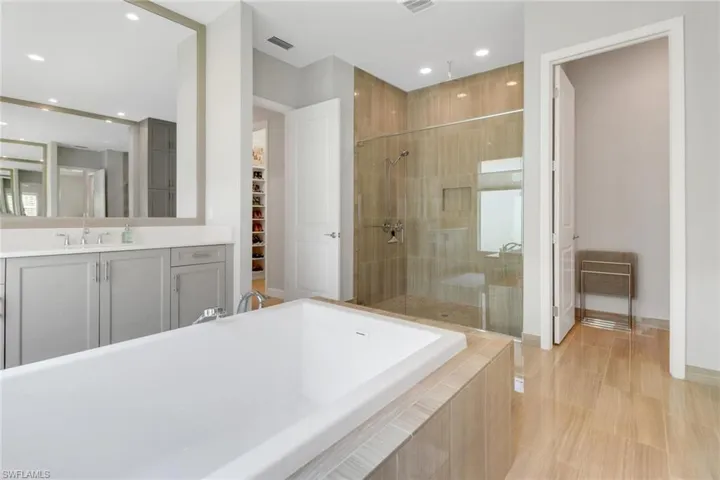 Full bath featuring tiled bath, visible vents, a spacious closet, a tile shower, and vanity