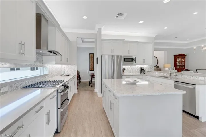 Kitchen featuring visible vents, appliances with stainless steel finishes, a peninsula, wall chimney range hood, and a sink