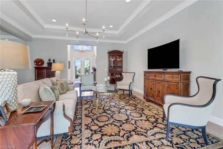 Living room featuring light wood-style flooring, a tray ceiling, a chandelier, and baseboards