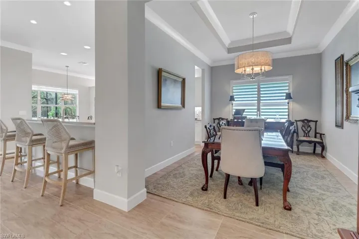 Dining room with recessed lighting, baseboards, ornamental molding, a tray ceiling, and an inviting chandelier