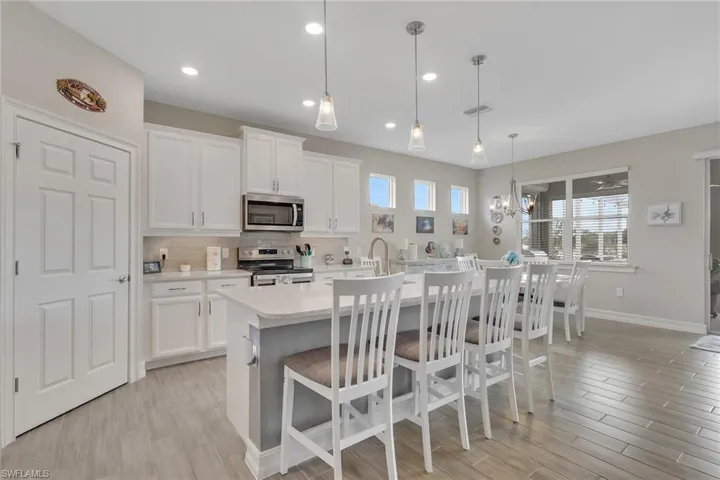 Kitchen featuring a kitchen bar, an island with sink, pendant lights, stainless steel appliances, and white cabinetry with crown molding