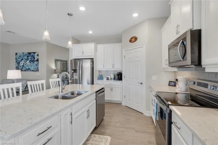 Kitchen with stainless steel appliances, tasteful backsplash, white cabinets, an island with sink, and a breakfast bar, corner walk in pantry