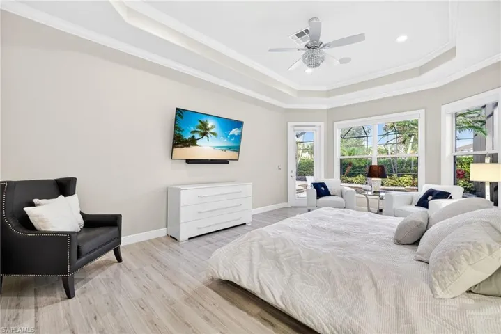 Primary bedroom with view of lanai and pool / spa,  featuring tile plank flooring, crown molding, tray ceiling, modern ceiling fan, and direct access to the lanai.