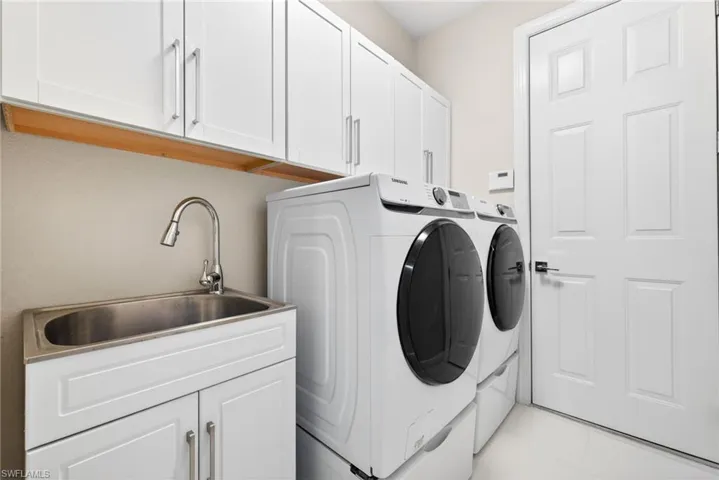 Laundry area includes utility sink, cabinets and front load washer and dryer.