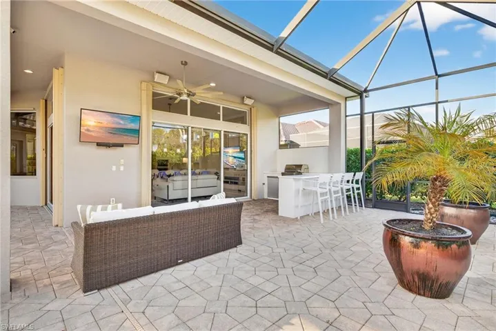 Entertaining area featuring an outdoor kitchen, seating area and tv.  Accordion storm protection shown on sliders