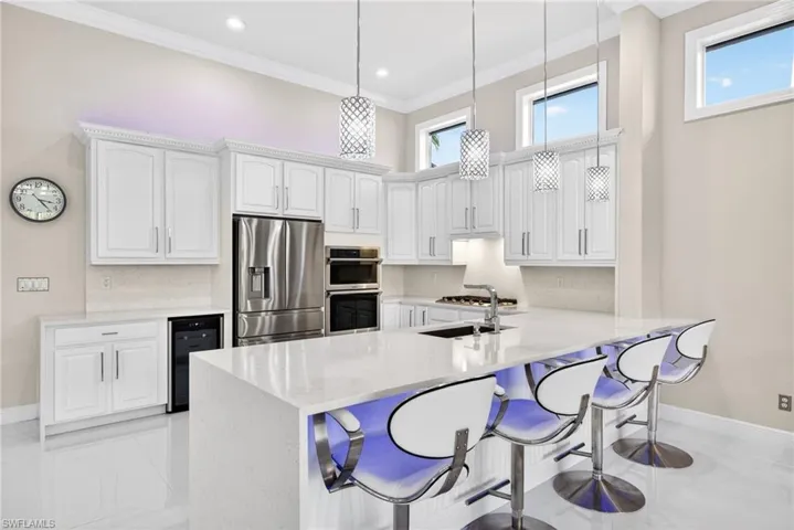 Kitchen featuring white cabinets, quartz countertops and backsplash,  a peninsula with seating for four, and pendant lighting.