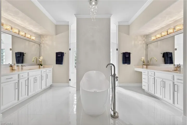 Primary bathroom featuring a bubbler tub, crown molding, dimensional white accent wall and two vanities with quartz countertops.  Walk-through shower featuring dual shower heads and a ceiling-mounted rainfall shower head for a spa-like experience.