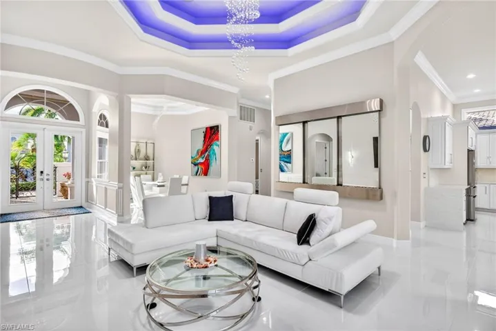 Living room featuring plenty of natural light, double entry doors, crown molding, a raised ceiling, and modern lighting.