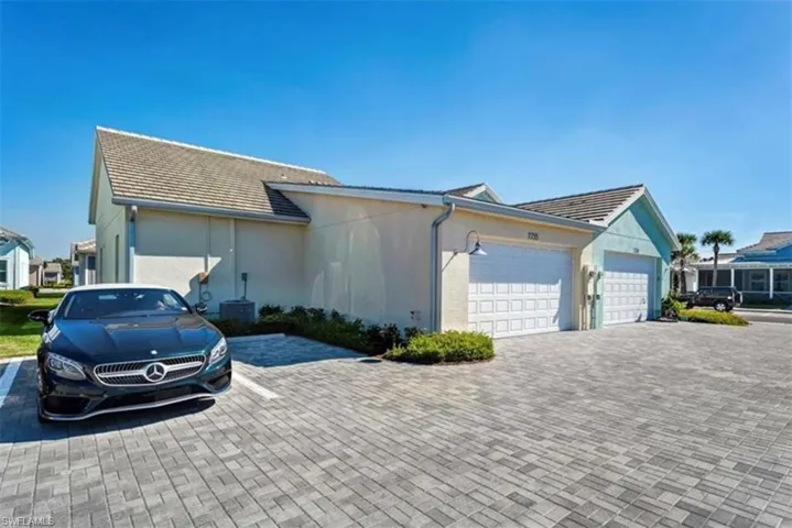 Paver driveway and parking area, stucco exterior, tiled roof, two single-car garages with panel doors, exterior wall-mounted lighting