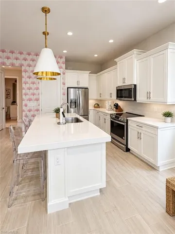 Bright kitchen featuring white cabinetry, a large center island with integrated sink, stainless steel appliances, recessed lighting, and wood-finish flooring
