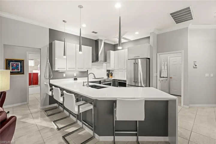 Kitchen with ornamental molding, appliances with stainless steel finishes, a breakfast bar area, white cabinets, and wall chimney range hood