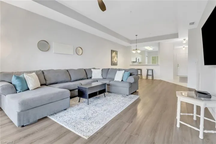 Living room with a raised ceiling, wood finished floors, ceiling fan, and a chandelier