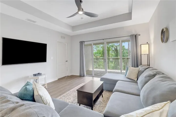 Living room with wood finished floors, a ceiling fan, baseboards, and a tray ceiling