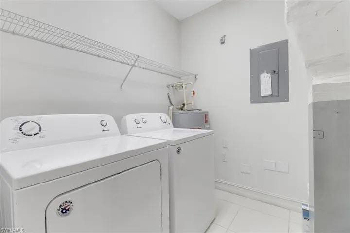 Laundry room with electric panel, washer and dryer, light tile patterned floors, baseboards, and water heater