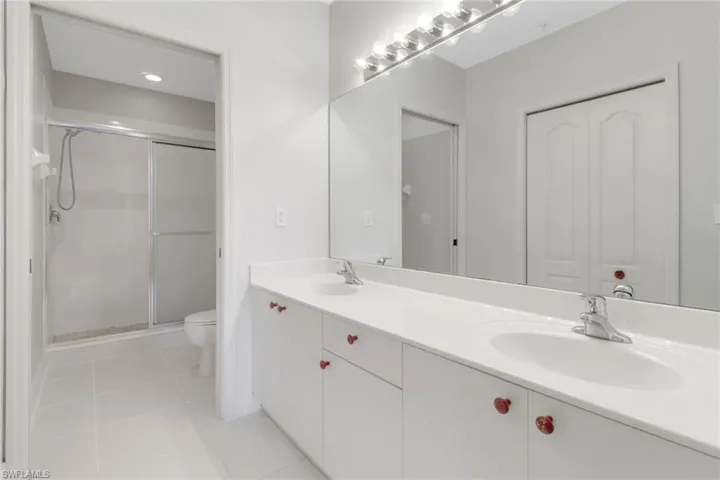 Full bathroom with toilet, double vanity, a shower stall, and tile patterned floors
